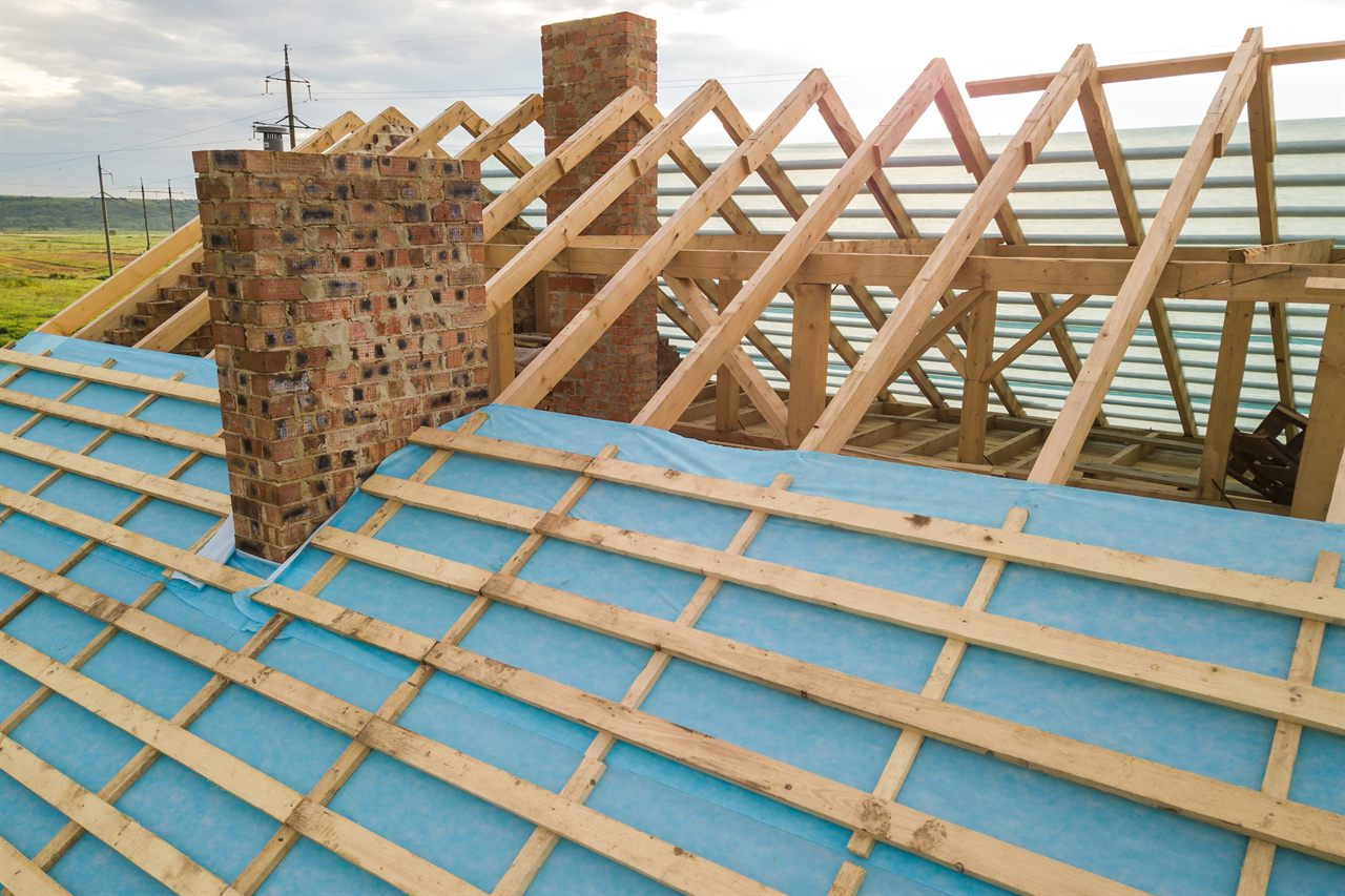 Hellend dak in renovatie met spantwerk, onderdakfolie en panlatten rond een schoorsteen